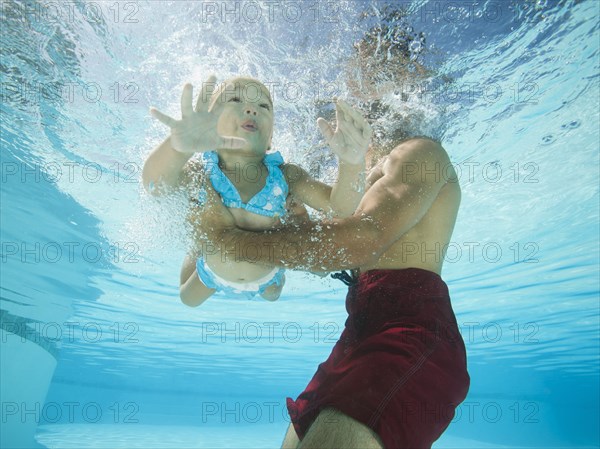 Mixed race father holding daughter in swimming pool