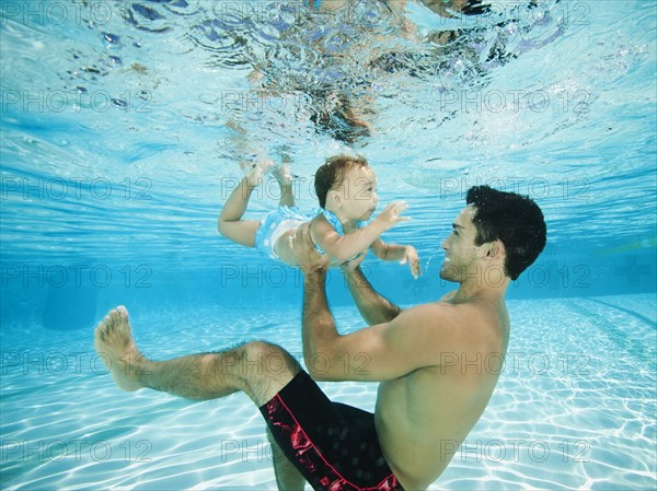 Father swimming underwater with daughter in swimming pool