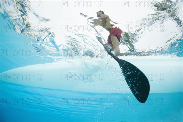 Mixed race man paddling on surfboard