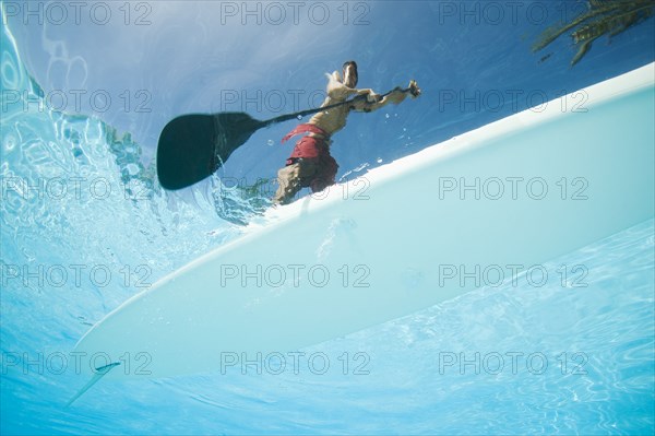 Mixed race man paddling on surfboard