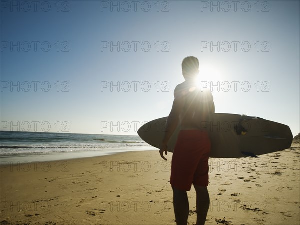 Mixed race man carrying surfboard on beach