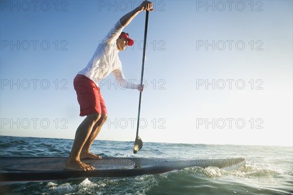 Mixed race man paddling on surfboard