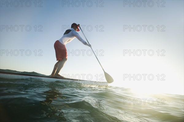 Mixed race man paddling on surfboard