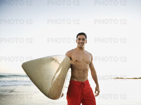 Mixed race man carrying surfboard on beach