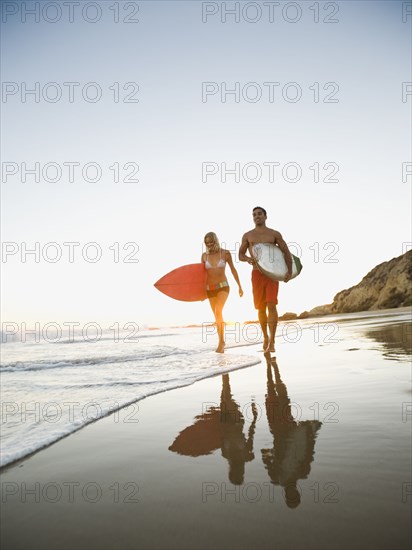 Couple walking on beach carrying surfboards