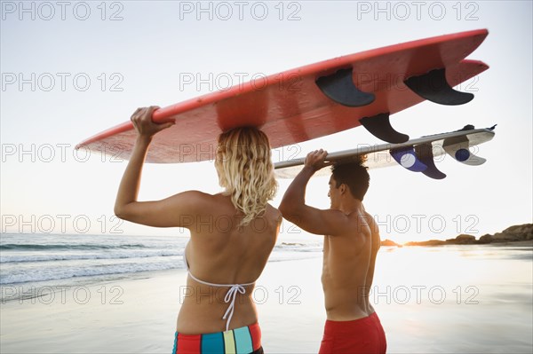 Couple walking on beach carrying surfboards