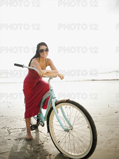 Hispanic woman riding retro bicycle on beach