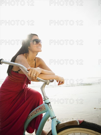 Hispanic woman riding retro bicycle on beach