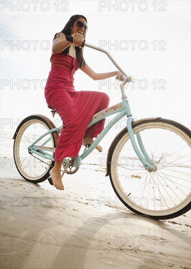 Hispanic woman riding retro bicycle on beach