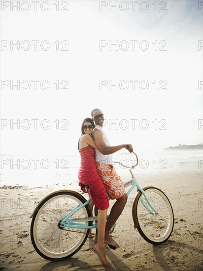 Couple riding retro bicycle on beach