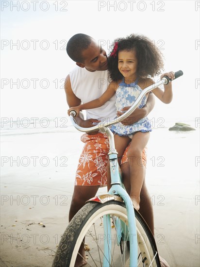 Black father helping daughter learn to ride retro bicycle