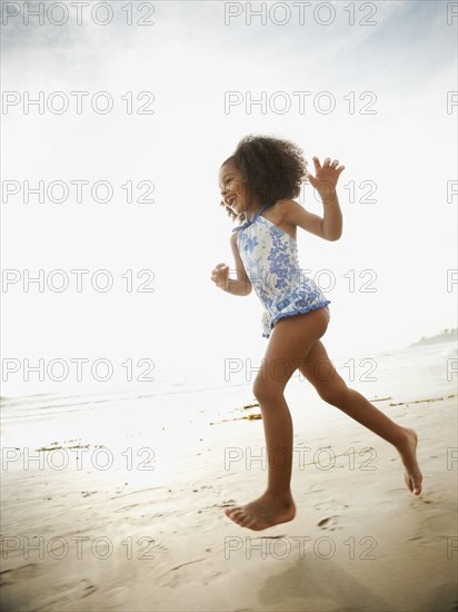 Mixed race girl in bathing suit running on beach