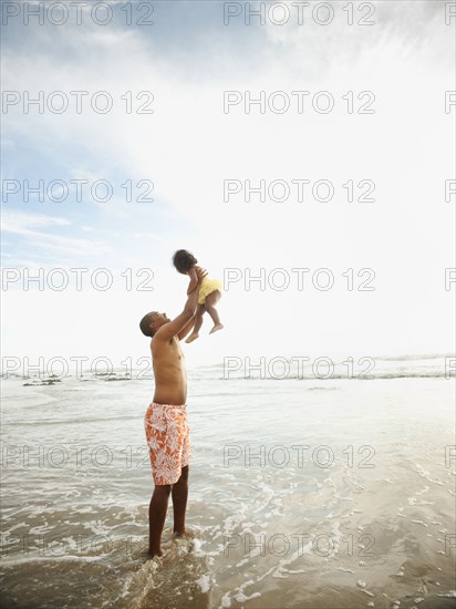 Black father lifting daughter while standing in ocean