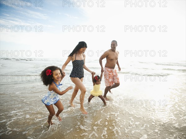 Family holding hands and wading through ocean water