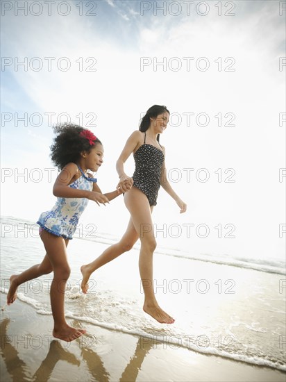 Hispanic mother and daughter holding hands and walking on beach