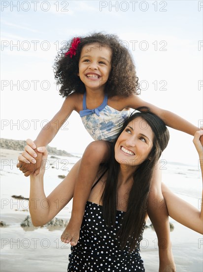 Hispanic mother carrying daughter on shoulders at beach