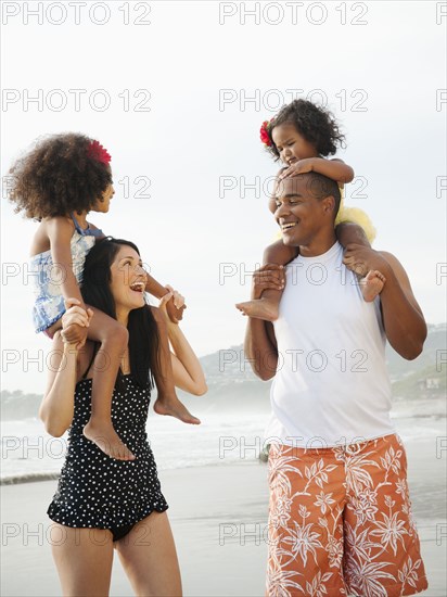 Parents carrying children on shoulders at beach