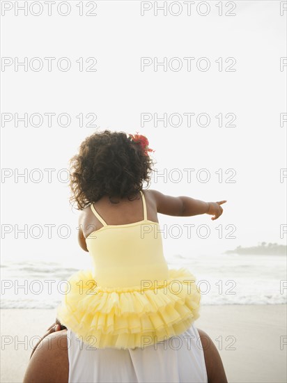 Black father carrying daughter on shoulders at beach