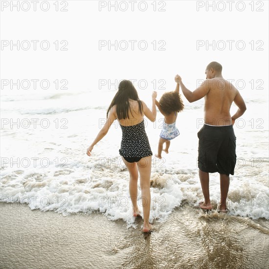 Parents swinging daughter between them on beach