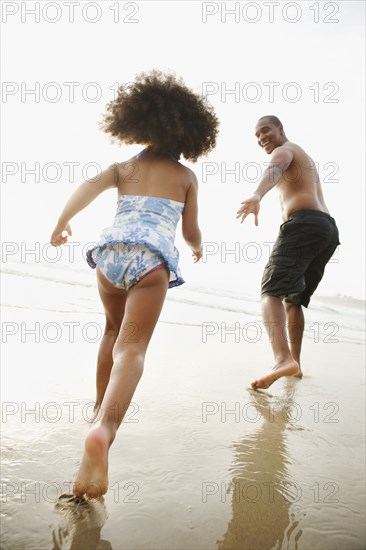 Black father holding out hand to daughter on beach