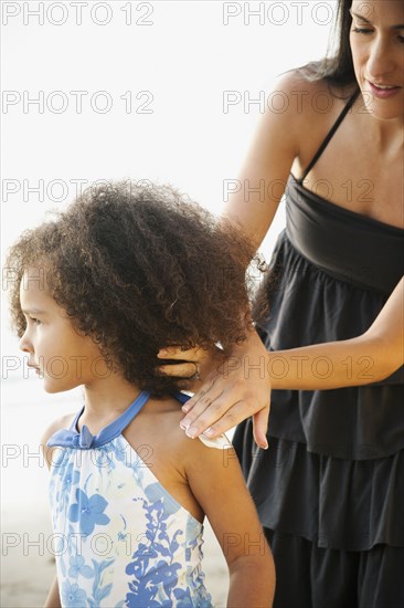 Hispanic mother rubbing sunscreen on daughter at beach