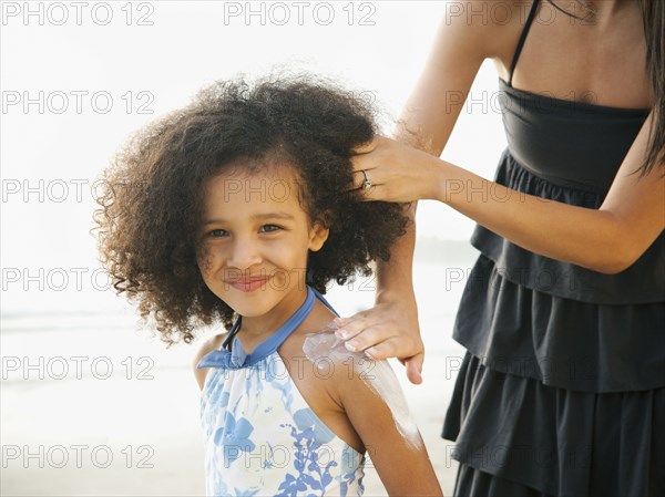 Hispanic mother rubbing sunscreen on daughter at beach