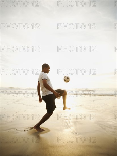 Black man playing with soccer ball on beach