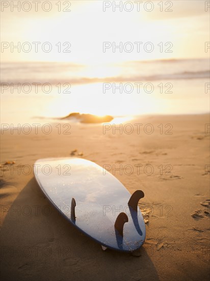 Surfboard laying on beach at sunset
