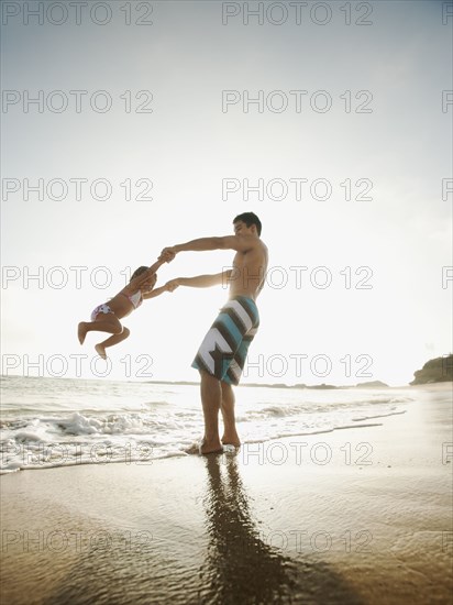 Mixed race father swinging daughter on beach