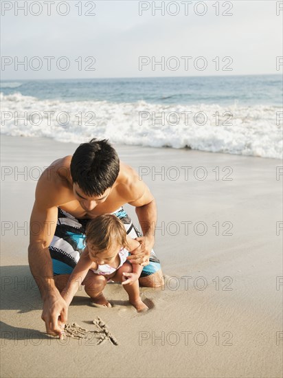 Mixed race father and daughter writing in sand together