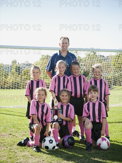 Coach and girl soccer players posing with trophy