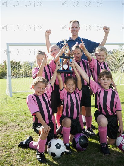 Coach and girl soccer players posing with trophy