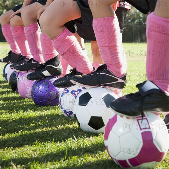 Girl soccer players standing with feet on soccer balls