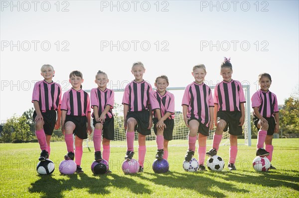 Girl soccer players standing with feet on soccer balls