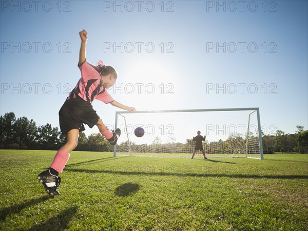 Girl soccer player kicking soccer ball at net