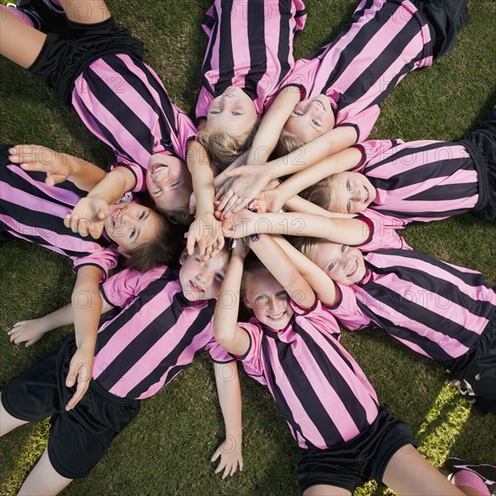 Girl soccer players laying in circle with arms raised