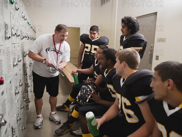 Coach talking to football players in locker room