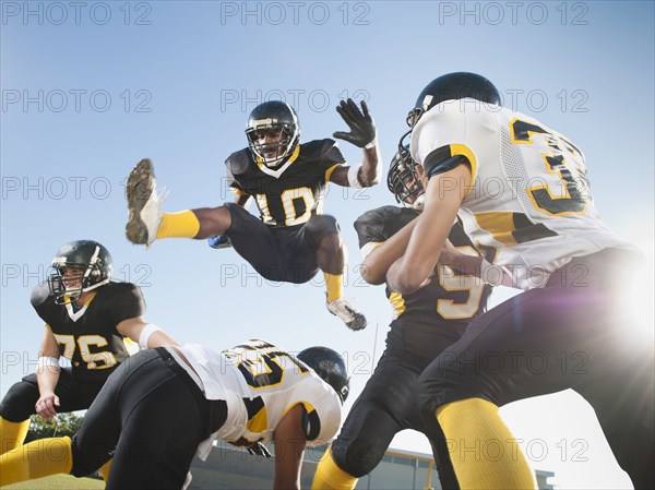 Football player leaping over players on football field