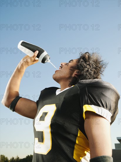 Hispanic football player drinking water