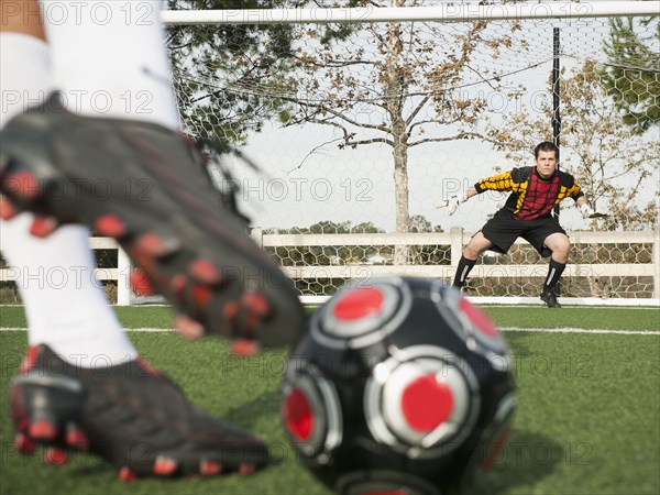 Soccer player kicking ball into goal on soccer field