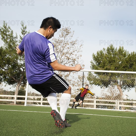 Soccer player kicking ball into goal on soccer field