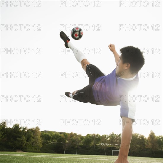 Asian soccer player in mid-air kicking soccer ball