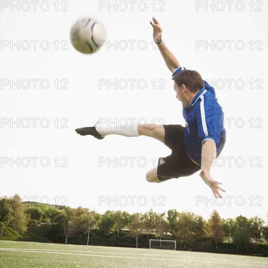 Caucasian soccer player in mid-air kicking soccer ball