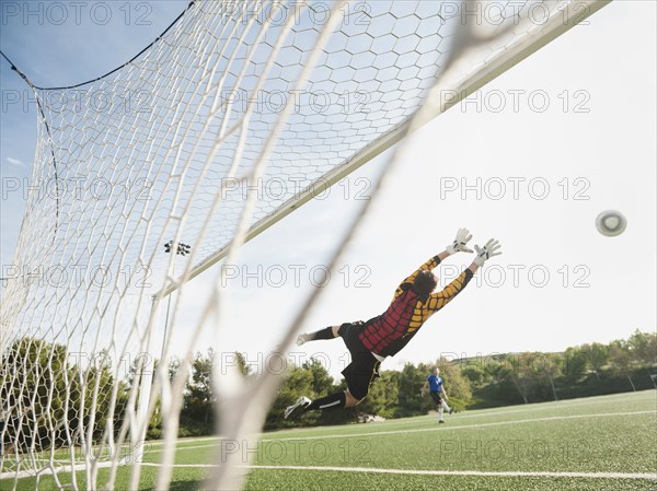 Mixed race goalkeeper in mid-air protecting goal