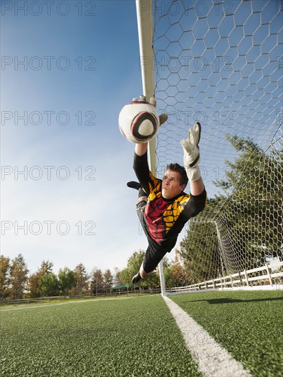 Mixed race goalkeeper in mid-air protecting goal