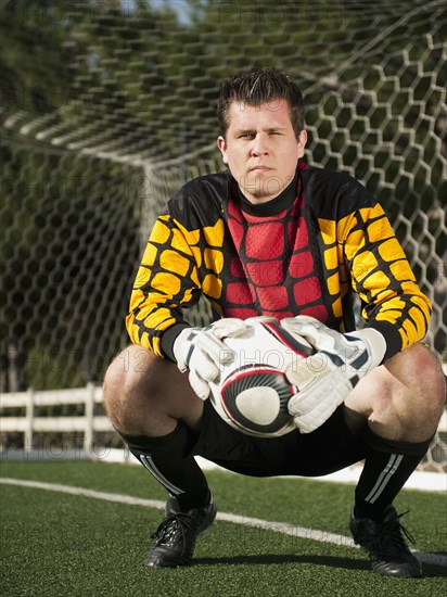 Mixed race goalkeeper crouching with soccer ball