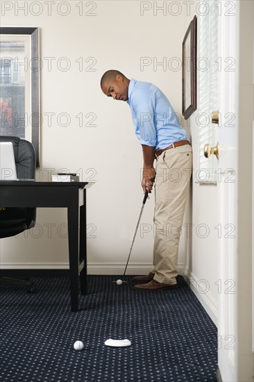 African American businessman putting golf ball