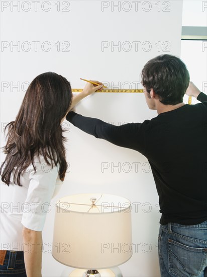 Couple marking wall with pencil and measuring tape