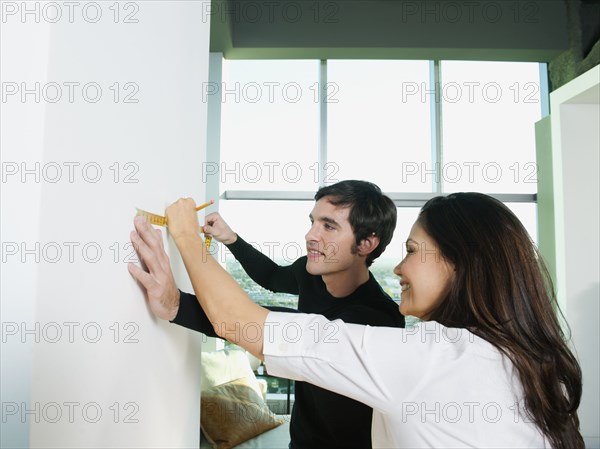 Couple marking wall with pencil and measuring tape