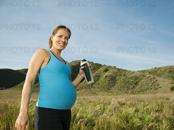 Pregnant Hispanic woman drinking water in remote area